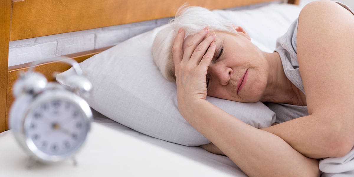 Older woman in menopause lying in bed with hand on forehead struggling to sleep with insomnia
