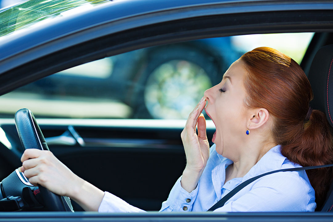 Sleep deprived woman yawning driving blue car