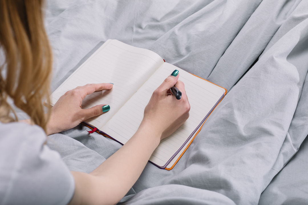 woman on bed writing in her Sleep Journal