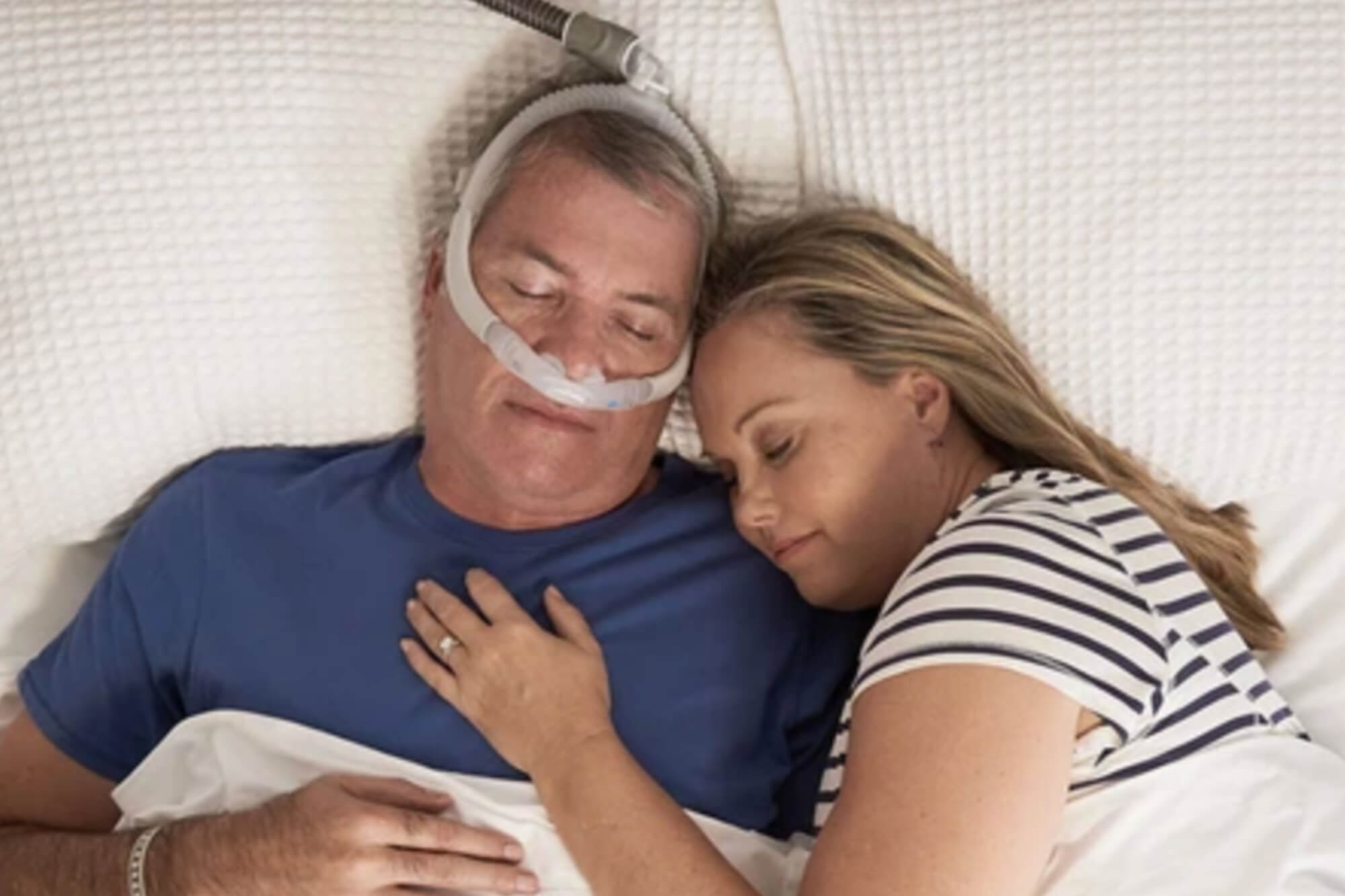 Couple Sleeping in Bed With Woman Cuddling Man While Sleeping With Nose Pillows CPAP Mask