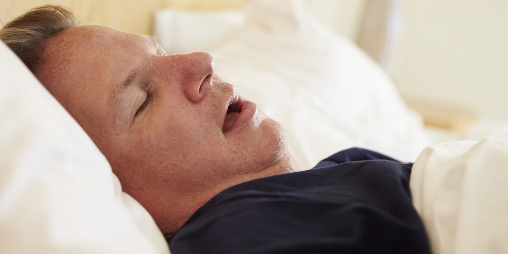 An overweight man asleep in bed snoring.