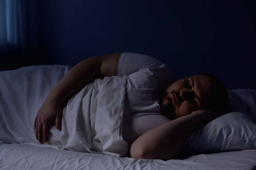 Overweight man sleeping on his side in bed.