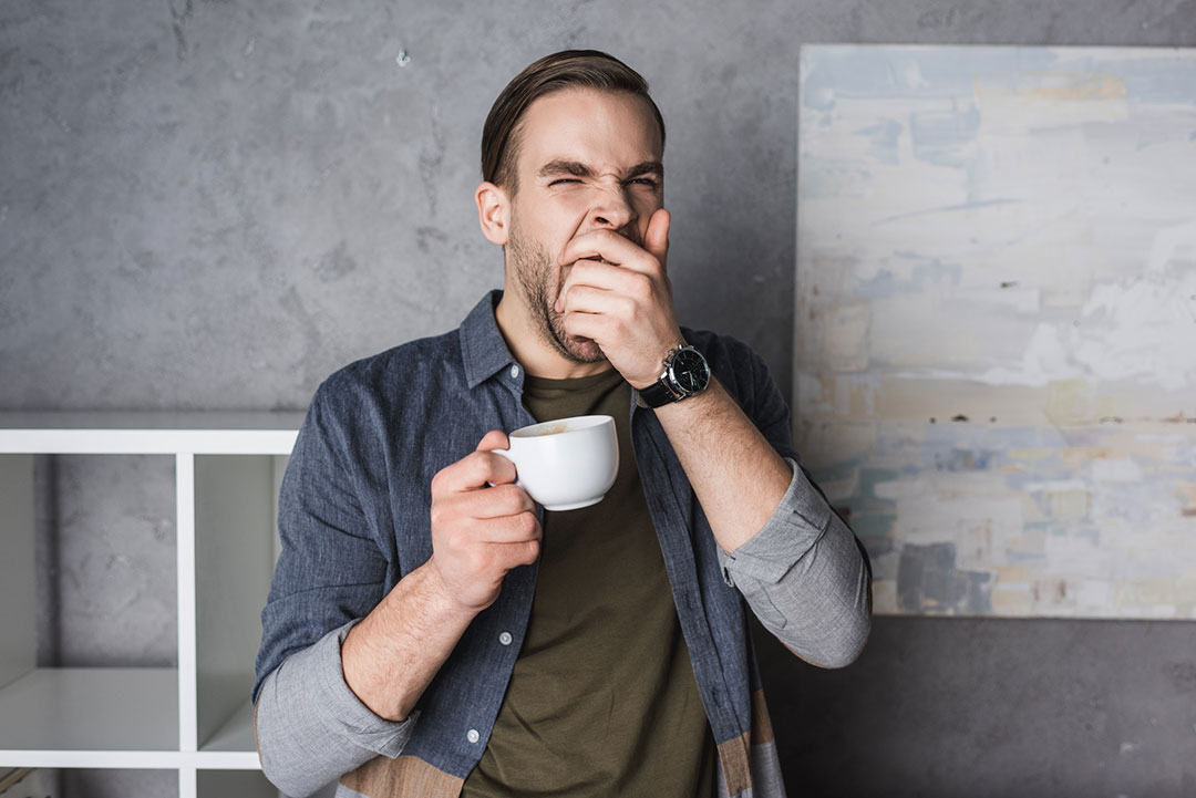 Exhausted Man Yawns Holding a Cup of Coffee