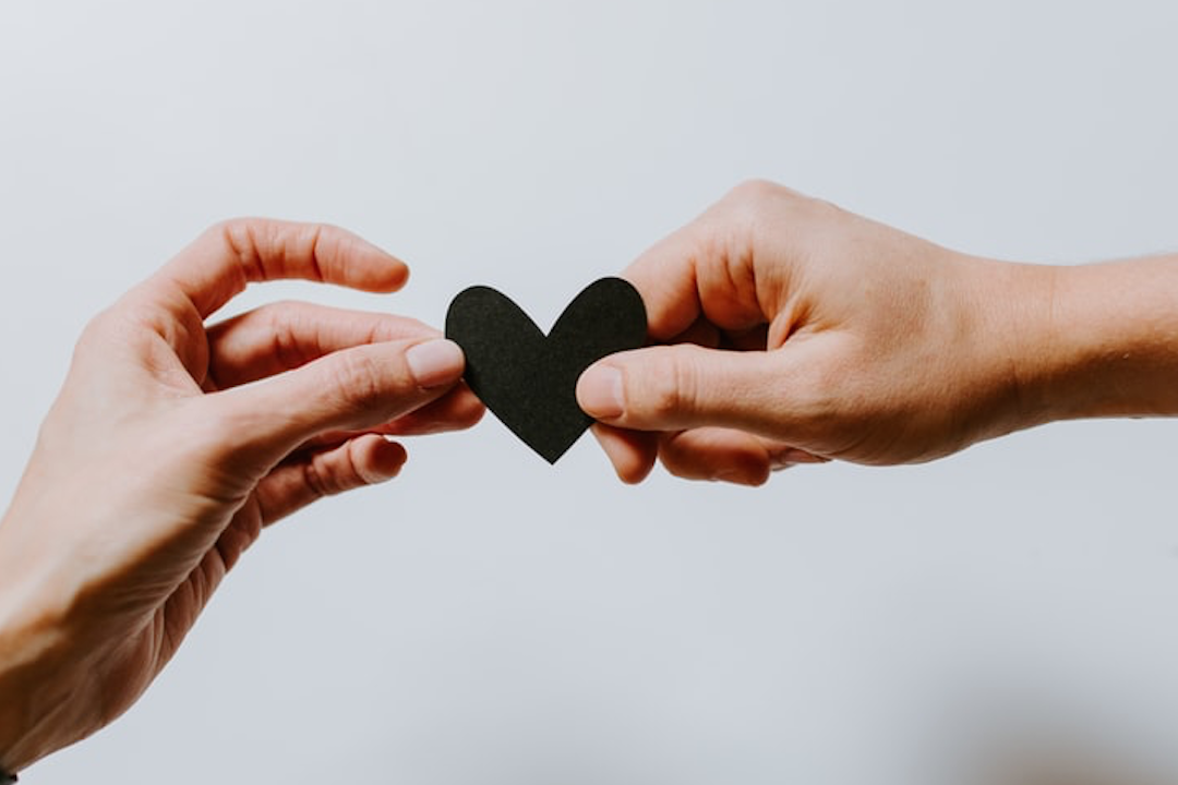 a black heart is being held by two female hands