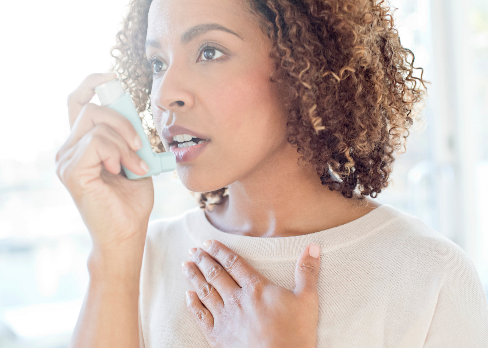 Woman with COPD in her 30s uses her inhaler while holding her other hand over her chest.