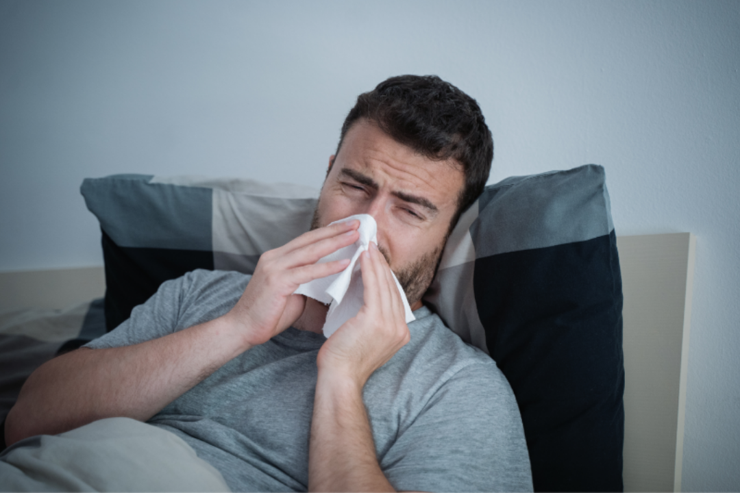 Man needing nighttime allergy relief lays in bed and blows his congested nose.