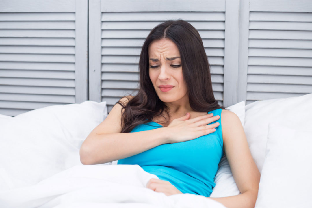 Young woman lying in bed with acid reflux discomfort