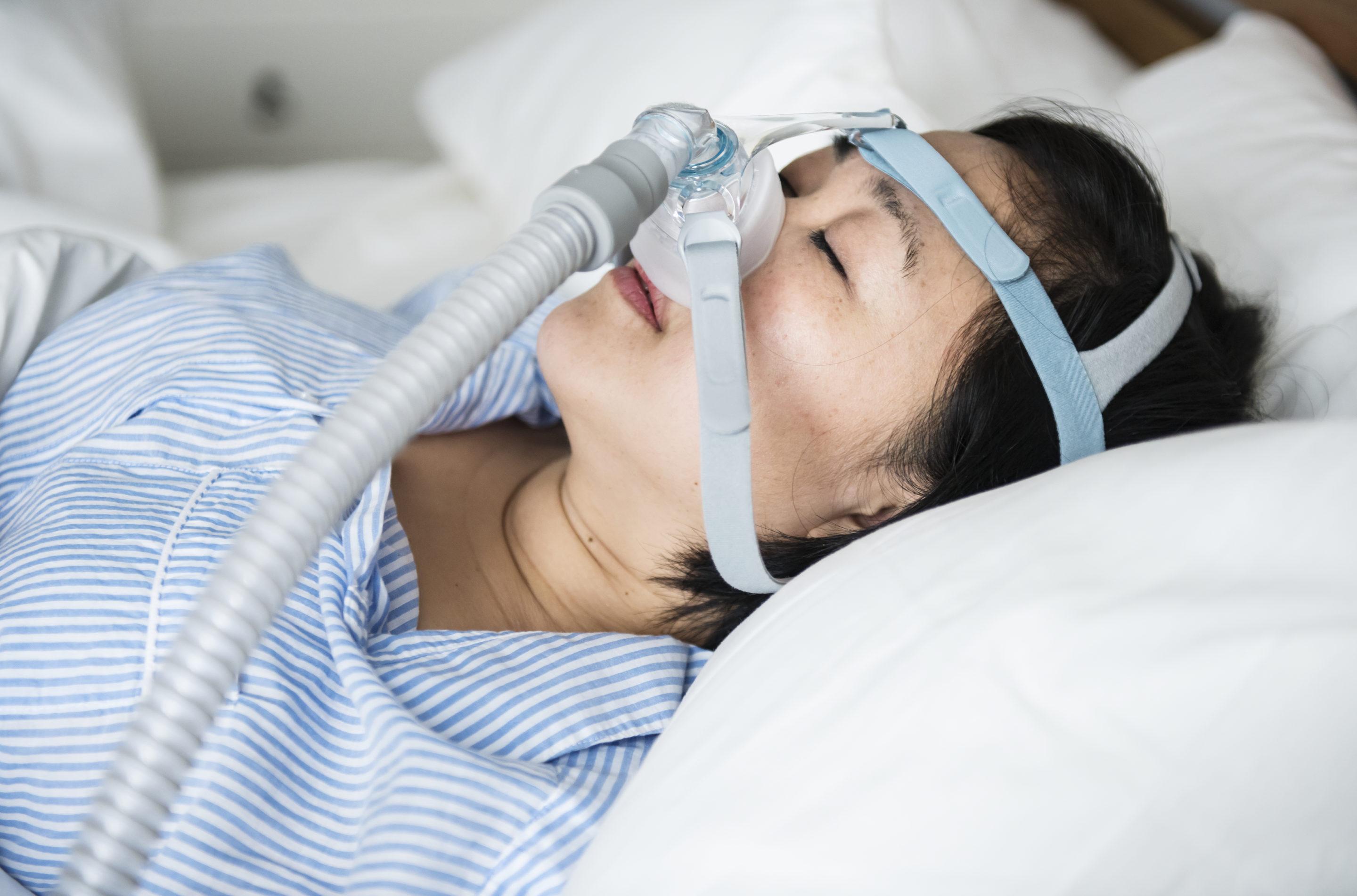 A sleeping woman wearing a CPAP mask in bed.