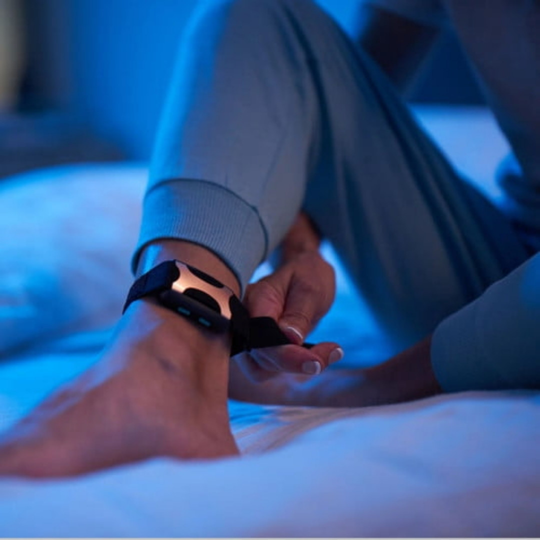 Woman fastens her Apollo stress relieving wearable around her ankle before bed