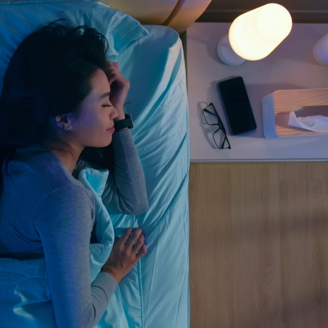 Woman sleeps soundly in bed next to her blue light blocking circadian rhythm light
