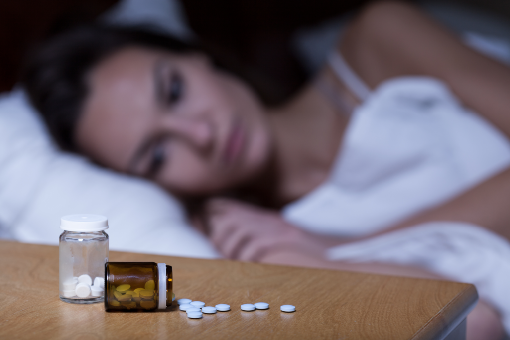 A tired woman staring at an overturned bottle of sleeping pills.