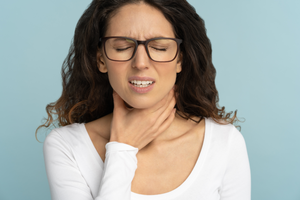 A woman with large tonsils clutching her throat.