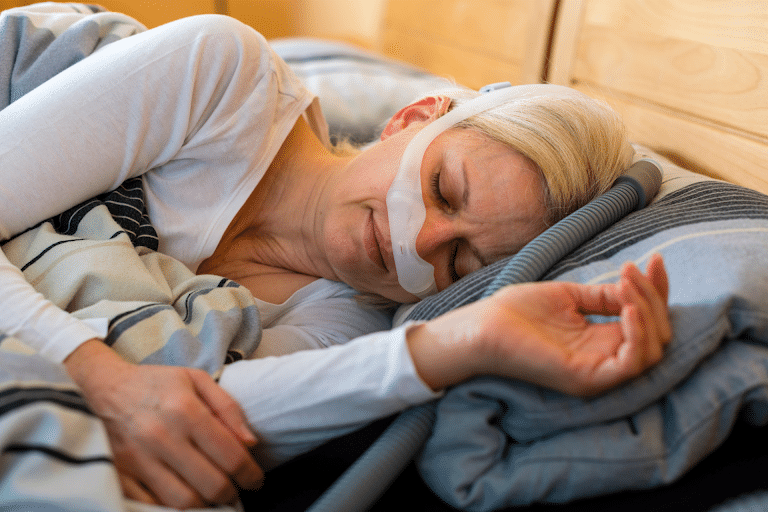 An older woman with obstructive sleep apnea sleeping in bed wearing a CPAP mask.