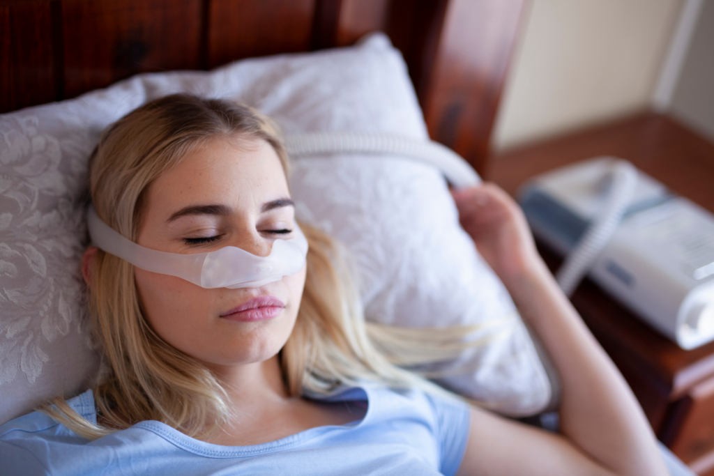 A woman wearing a CPAP mask sleeping in bed.
