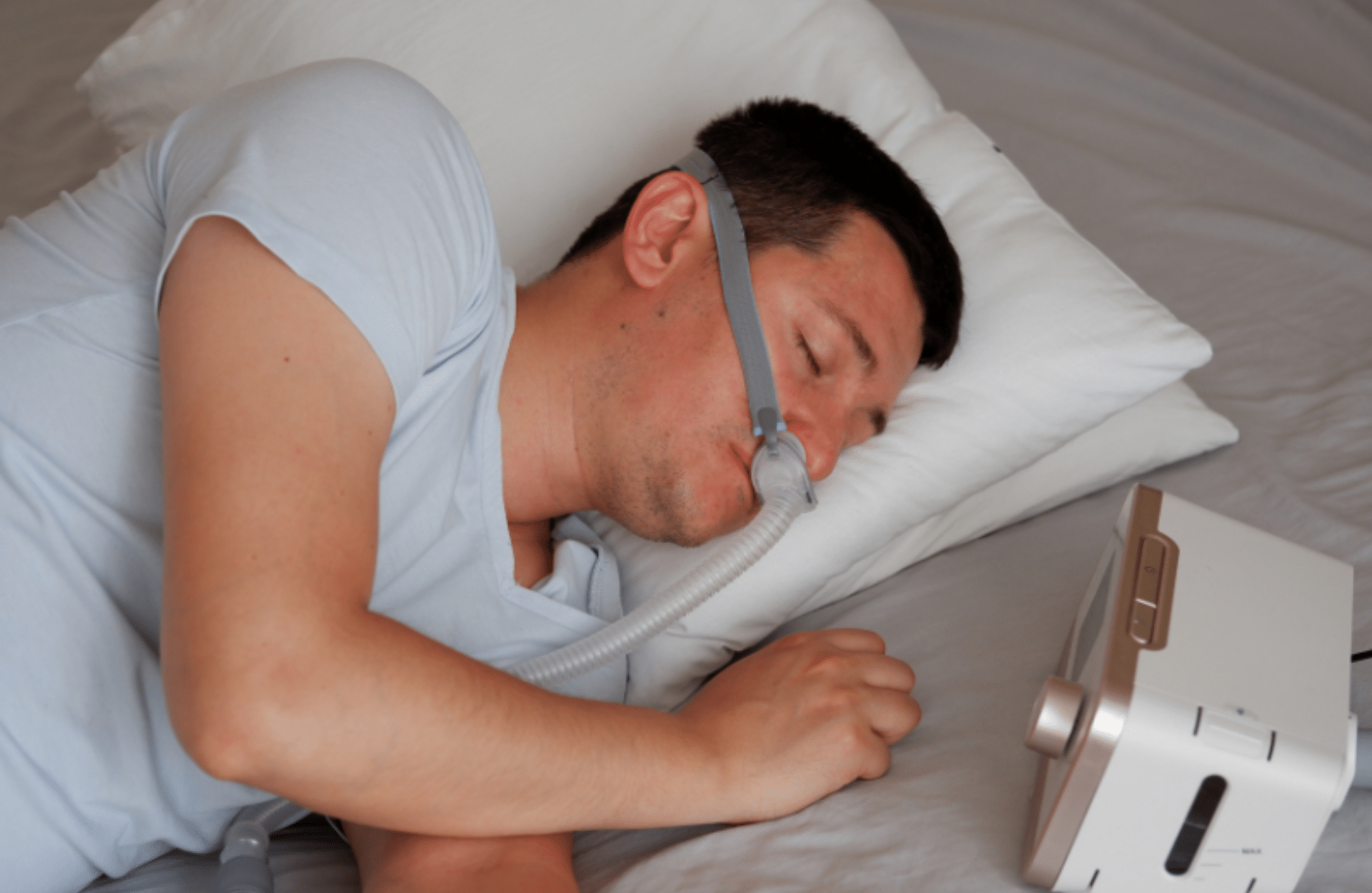 A man wearing a CPAP mask sleeping on his side in bed.