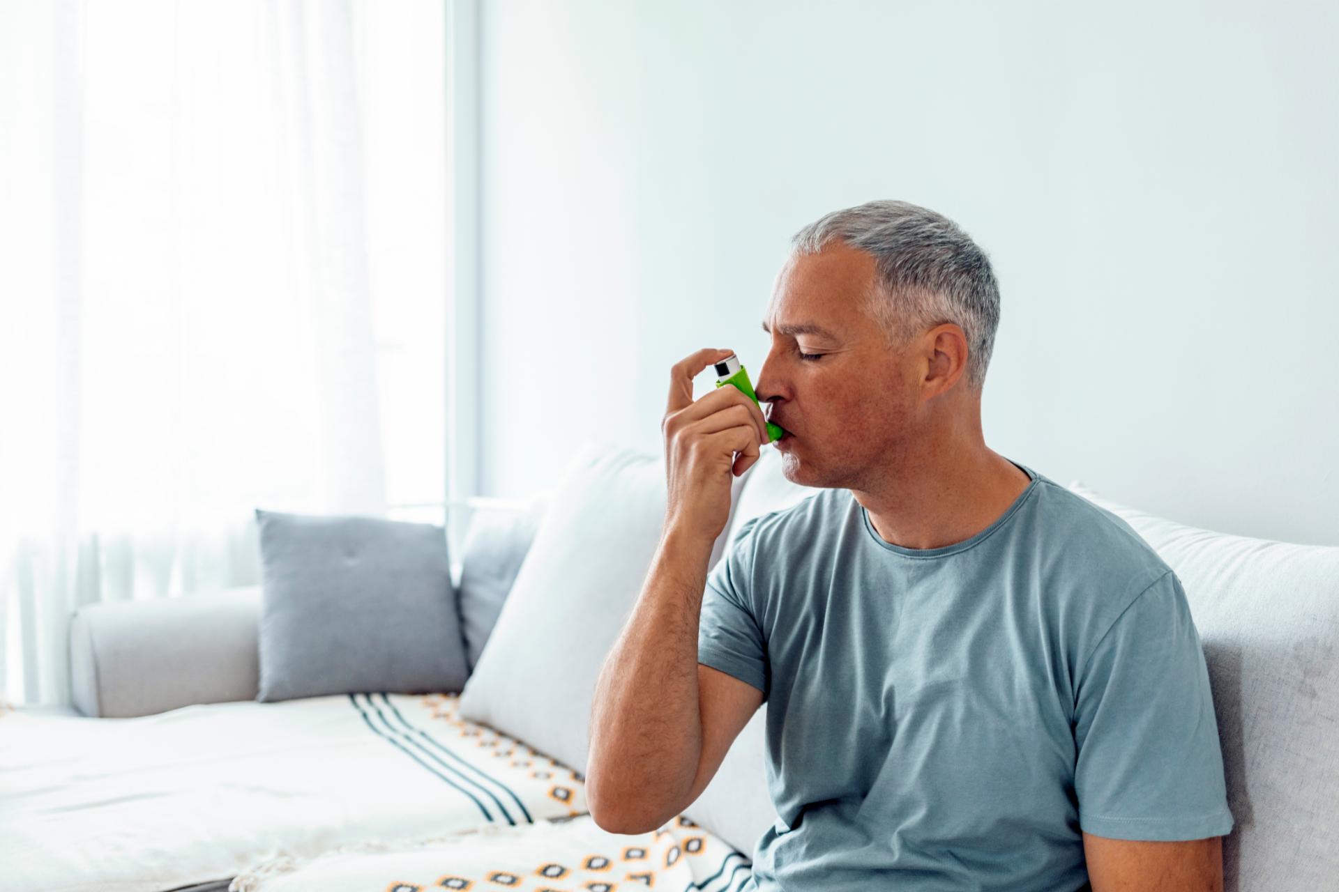 An older man with asthma using a rescue inhaler in bed.